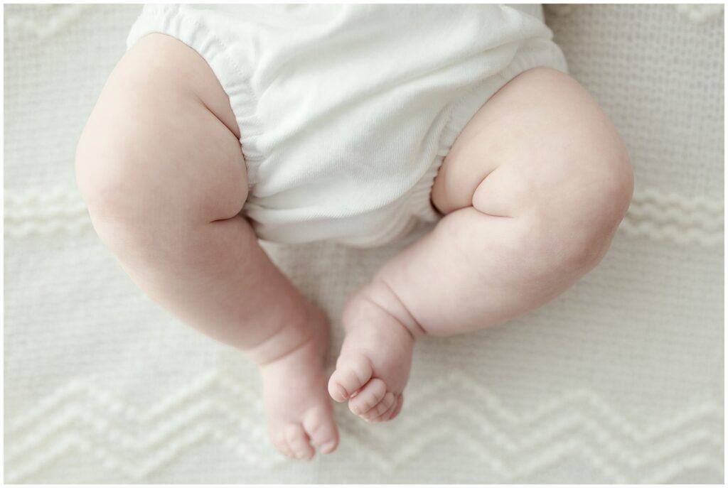 Soft baby thighs and feet in a white diaper on a cozy cream blanket, showcasing newborn photography by Mary Christine Photography.