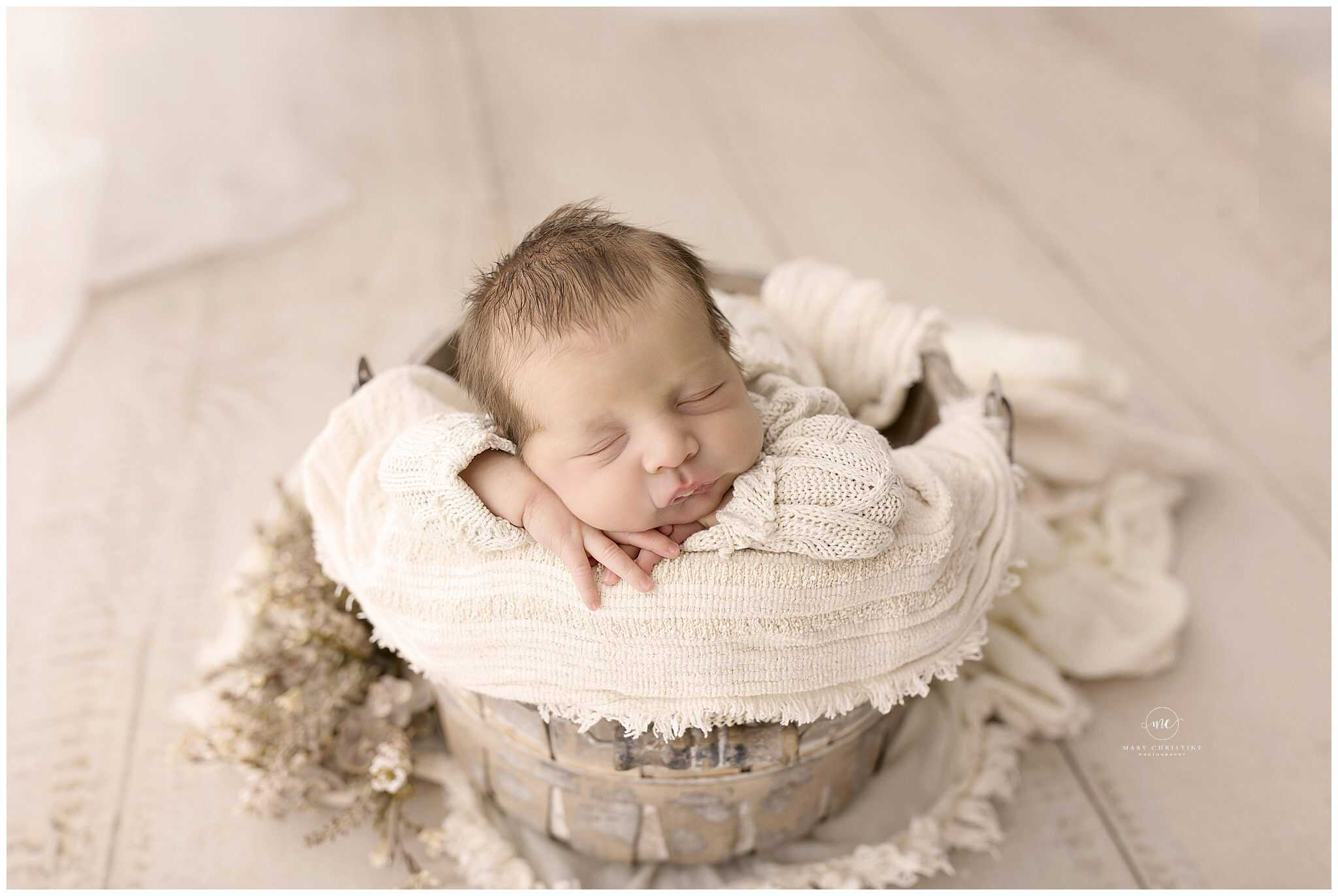 Soft-focused newborn baby sleeping in a rustic basket with cozy cream knitted blanket, ideal for capturing delicate newborn photography.