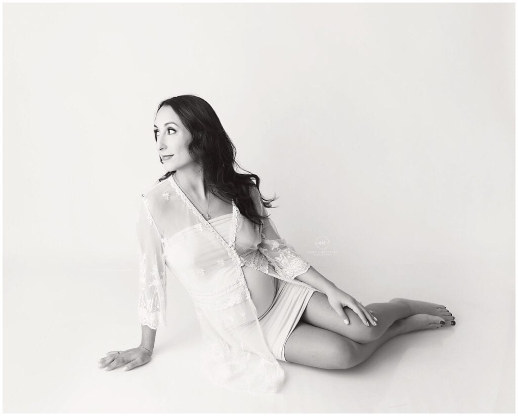 Elegant black and white portrait of a woman sitting on the floor, wearing a silky slip dress and a sheer lace robe, captured by Mary Christine Photography.