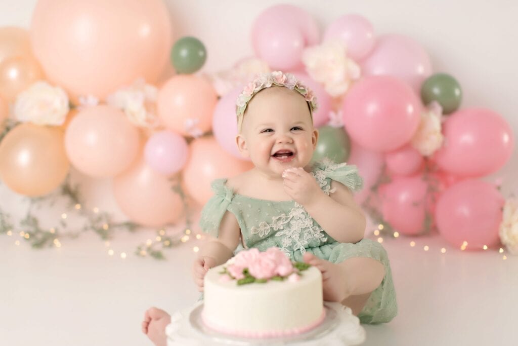 Vibrant baby birthday celebration with pastel balloons, floral accents, and a smiling toddler in a mint green dress. Perfect for children's event photography focusing on joyous milestones.