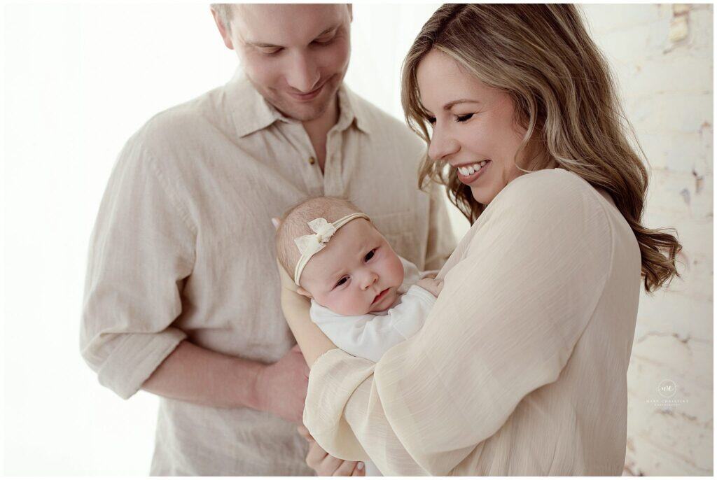 Beautiful family portrait of parents holding their adorable newborn girl in a bright, airy studio setting, capturing love and tenderness in a professional newborn photography session.