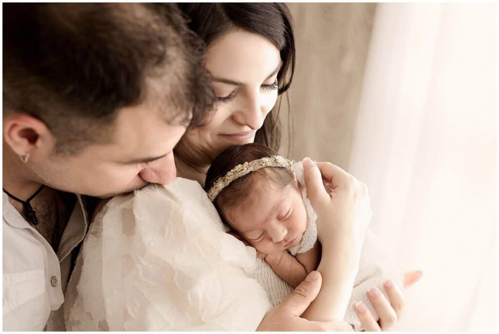 Soft focus image of a family celebrating the joy of welcoming a new baby girl, capturing tender moment of parents holding sleeping infant, natural window light, warm neutral tones, professional newborn photography by Mary Christine Photography.