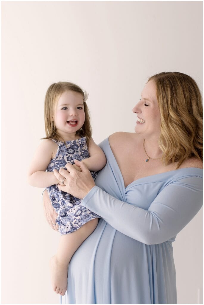 Soft-focused portrait of a happy mother holding her young daughter, both smiling, in a professional studio setting, showcasing family love and portrait photography.