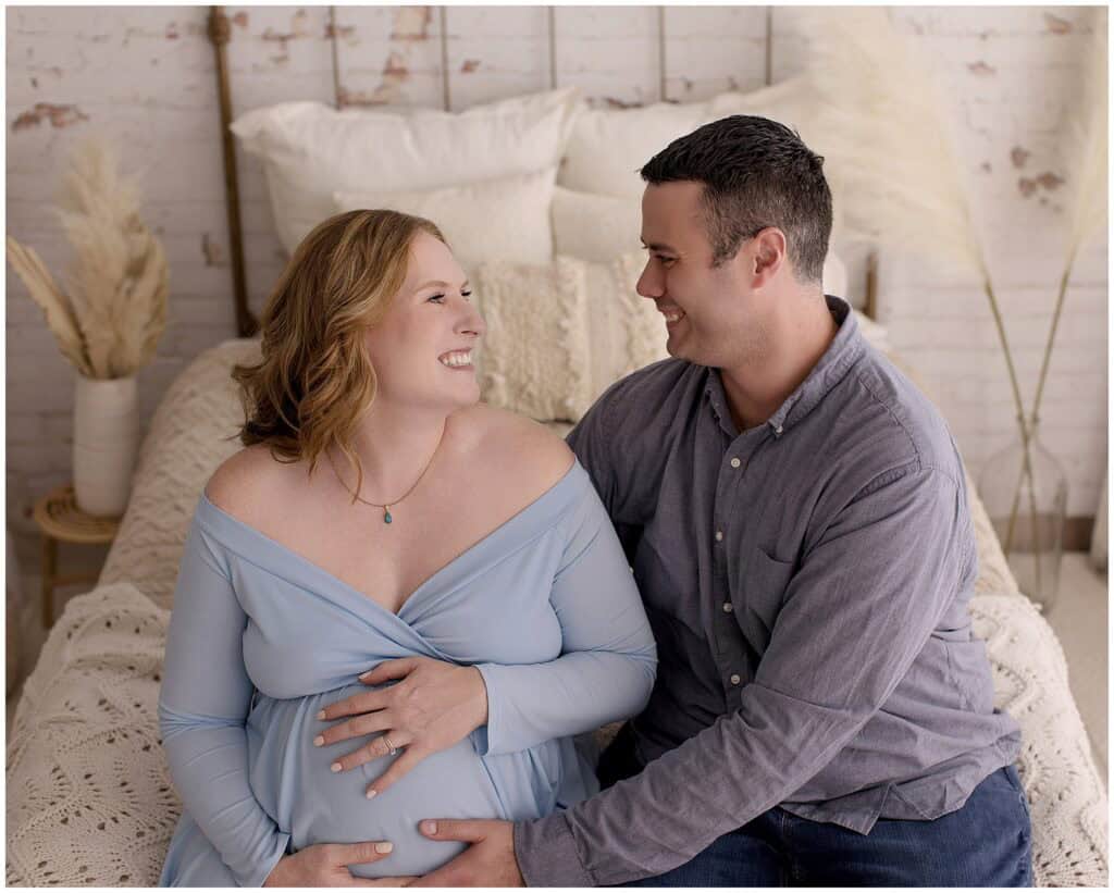 Pregnant woman and her partner smiling, capturing a heartfelt maternity photoshoot, emphasizing couple love, family photography, and maternity photography in a cozy, well-lit indoor studio setting.
