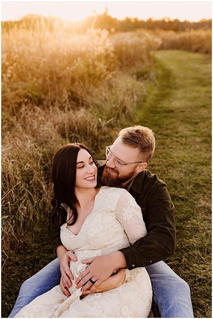 What to wear for maternity photos; a couple sitting in a field for their maternity photos at sunset
