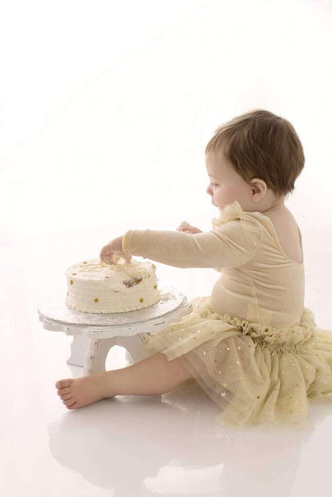 Side view of baby girl during a cake smash session reaching into her birthday cake