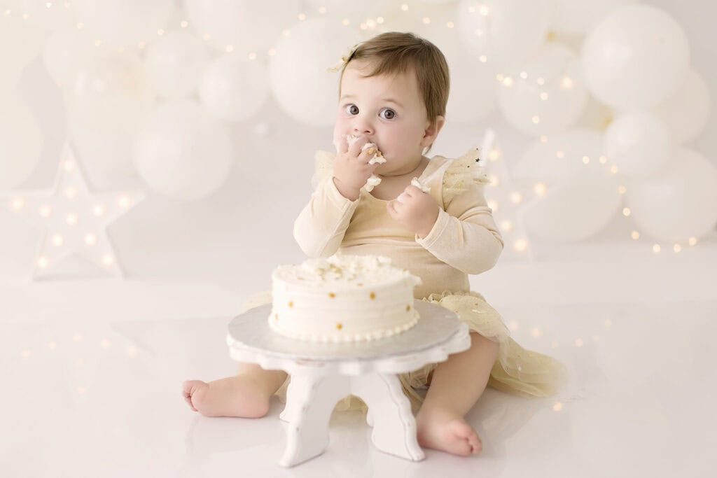 Baby girl enjoying her first birthday cake smash session with a simple neutral setup