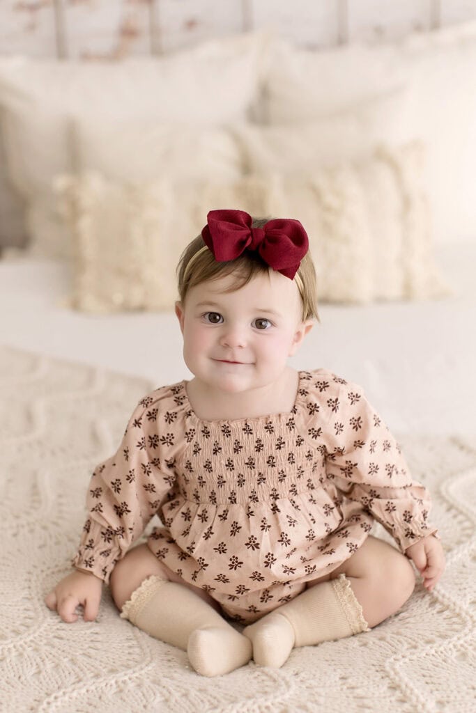 Baby girl sitting during a milestone photo session in Medina Ohio wearing a neutral outfit and red bow