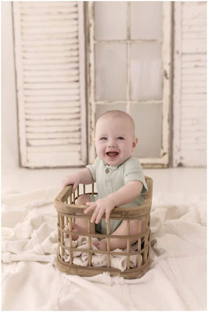 Smiling baby boy sitting in a wooden basket during a milestone photography session