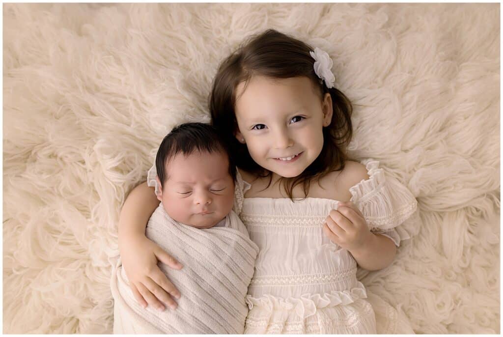 Big sister holding newborn baby boy during studio newborn photos